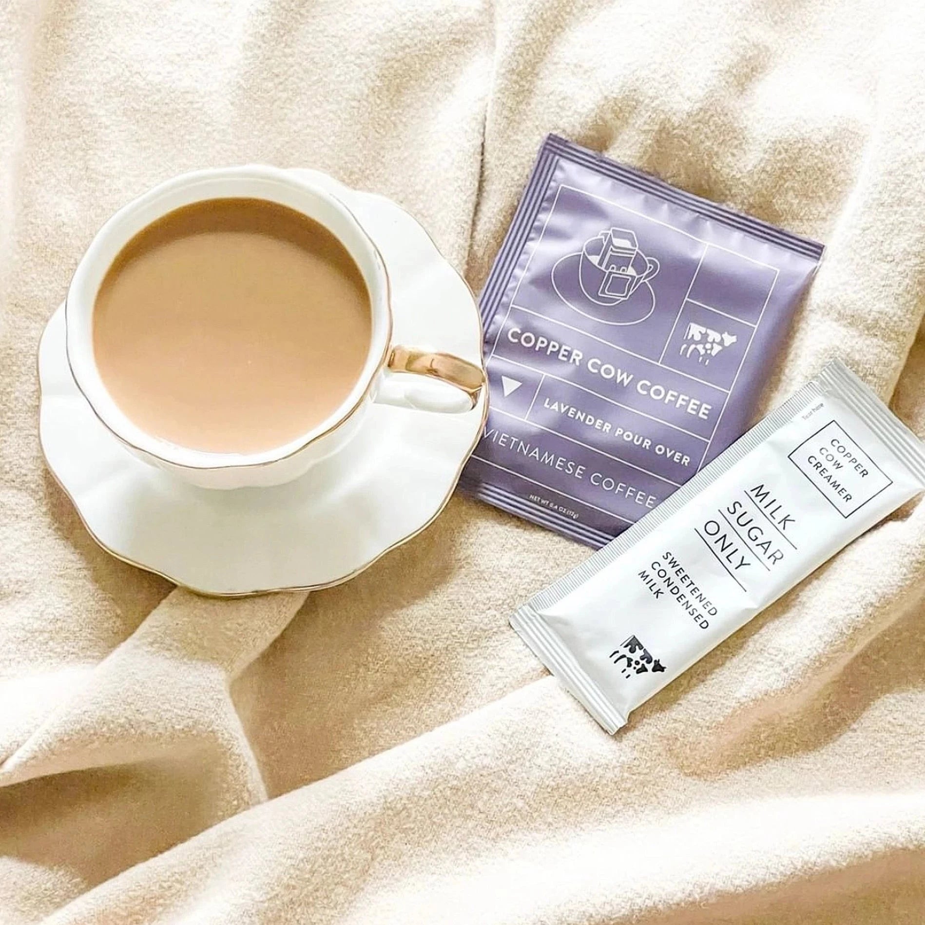 white mug with coffee. mug has purple sachet containing coffee and sweetened condensed milk aches next to it