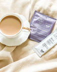 white mug with coffee. mug has purple sachet containing coffee and sweetened condensed milk aches next to it