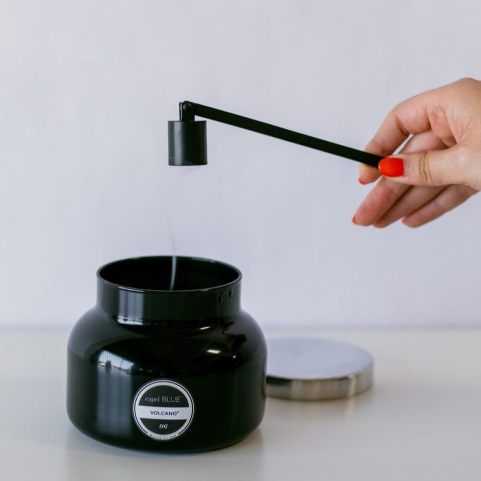 Black candle snuffer above a black candle with a stream of smoke coming off the wicks.