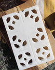 white breeze block ice pack on piece of wood in a picnic setting. Ice pack has cut outs resembling mosaic pattern