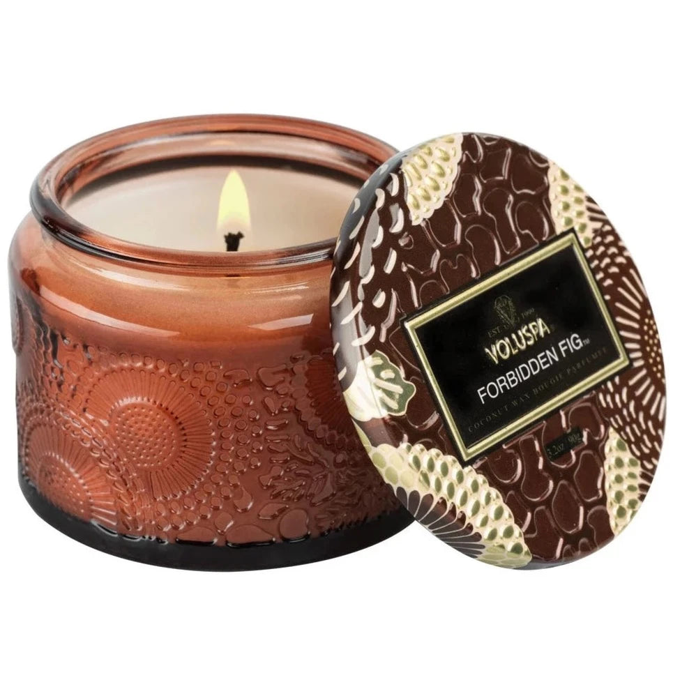 Amber colored petite glass jar candle - forbidden fig scent. Candle burning on white background.