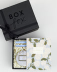 BOXFOX black Gift Box containing Rifle Paper Hydrangea Pocket Notebooks, 2 Periwinkle Le Pens, and Voluspa Mokara Petite Glass Jar Candle.