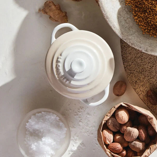 Eggshell colored cocotte on table next to bag of nuts and bowl of salt