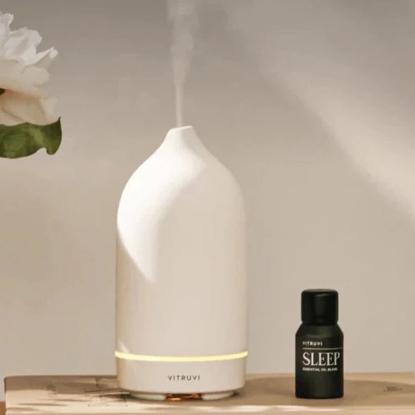 White Stone Essential Oil Diffuser sits on top of book next to Sleep oil and vase of flowers