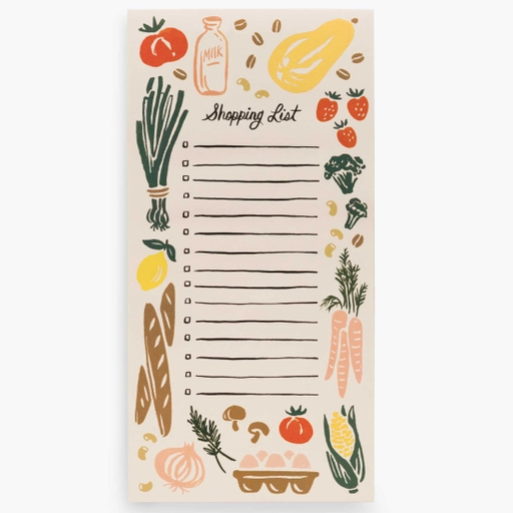 Beige colored note pad with "Shopping List" in black cursive text on top with colorful produce depictions around edges. Photographed against white background.