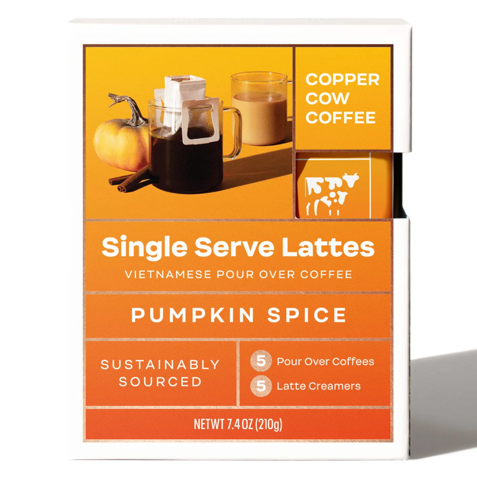 A square box with yellow to deep orange gradient and picture of pour over tablescape in top right with a small pumpkin, clear coffee mug with pour over filter on top, and a clear coffee mug with a latte. Text on box reads, "Copper Cow Coffee Single Serve Lattes Vietnamese Pour Over Coffee Pumpkin Spice Sustainably Sourced 5 Pour Over Coffees 5 Latte Creamers Net Wt 7.4 OZ (210g). Photographed on white background. 