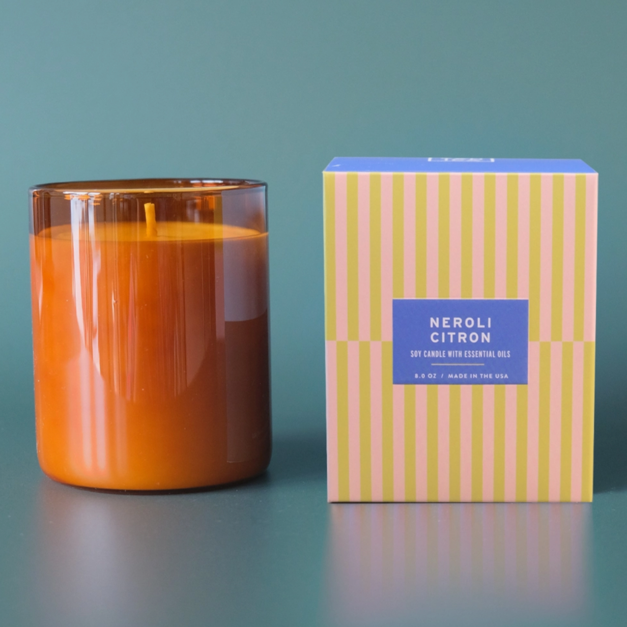 amber glass candle with striped box next to it behind blue background