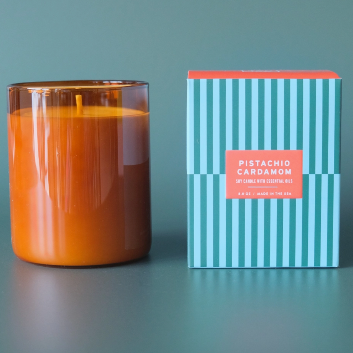 amber glass candle next to striped blue box behind teal background