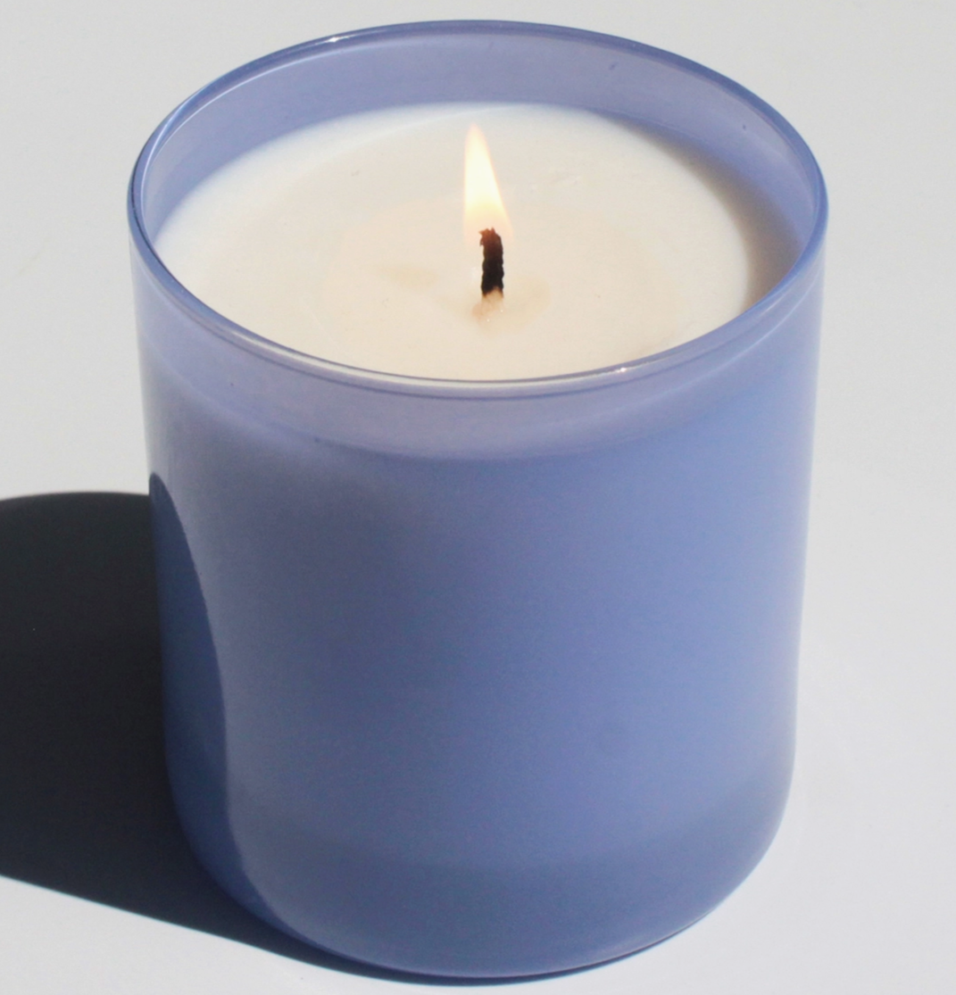 purple glass candle burning behind white background 