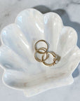 Ceramic seashell trinket tray holding 3 gold rings against a white marbled background