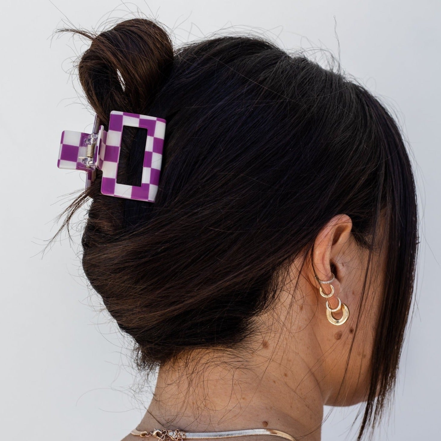 Girl with dark brown hair wearing a purple and white mini square claw clip against a white background