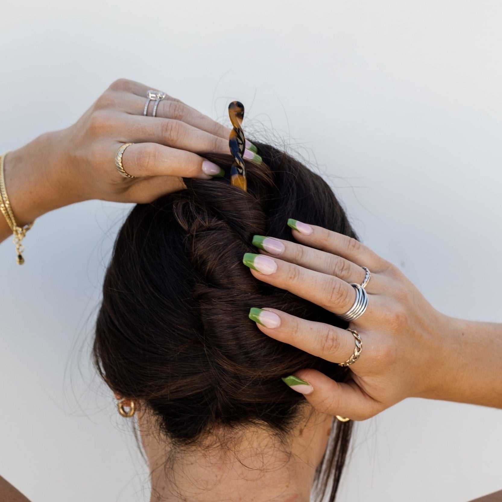 Girl with dark brown hair wearing a twisted updo with a brown tortoise hair stick against a white wall background