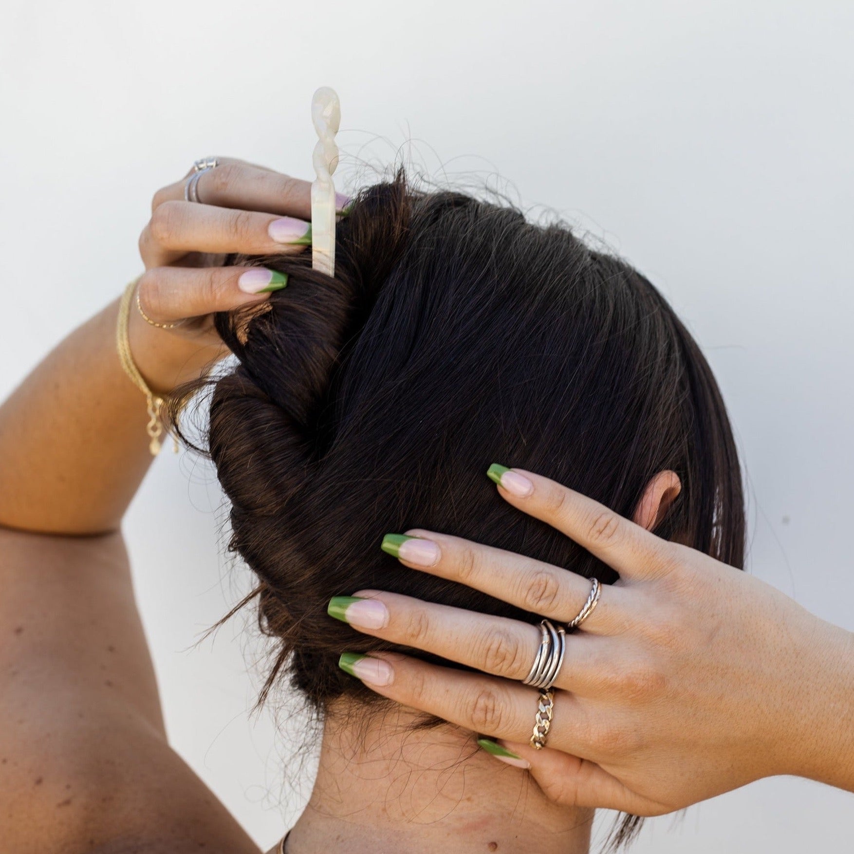 Girl with dark brown hair wearing a twisted updo with a white marble hair stick against a white wall background